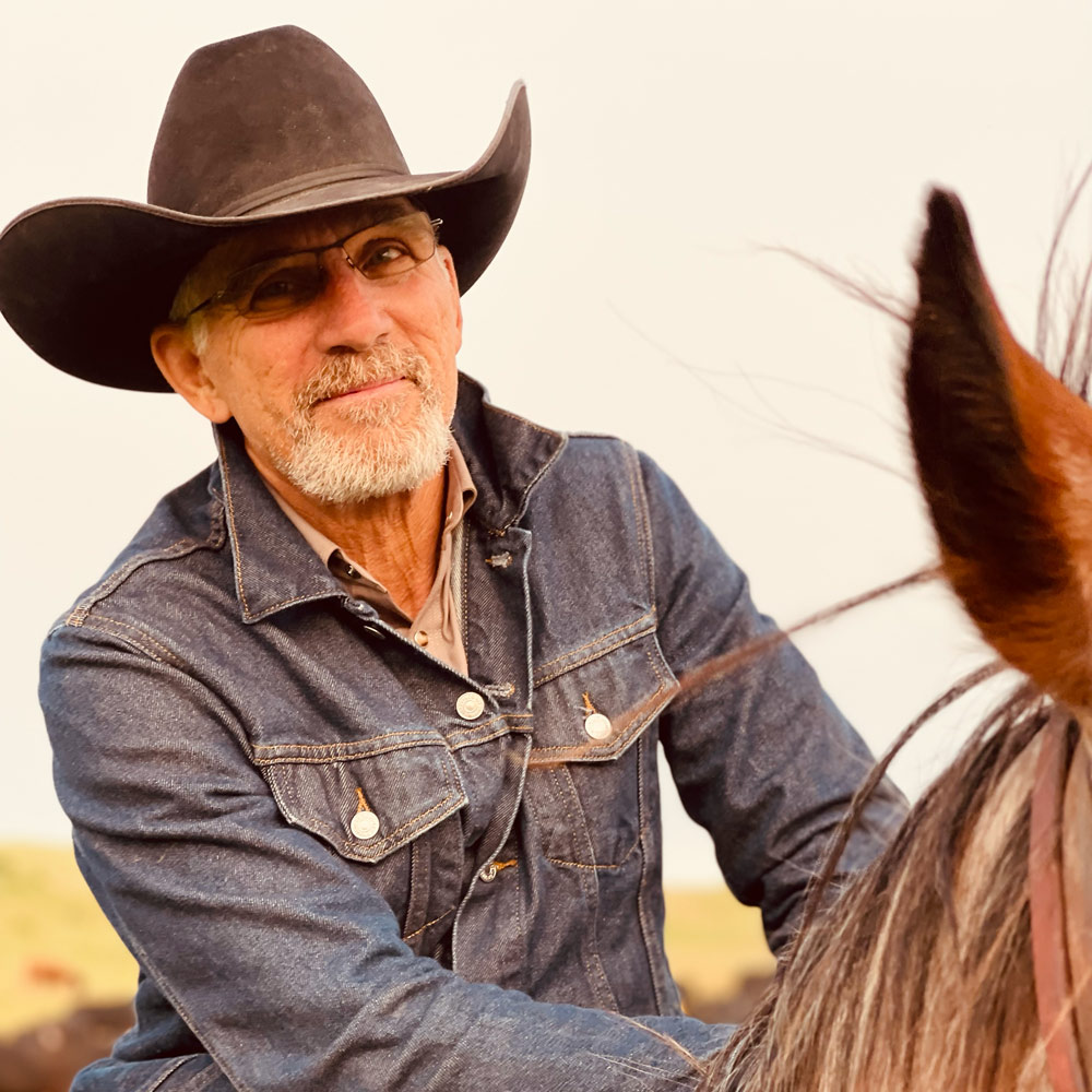 Headshot of Parable Pictures team member Peter Robbins wearing his glasses, a cowboy hat and denim button-down on horseback