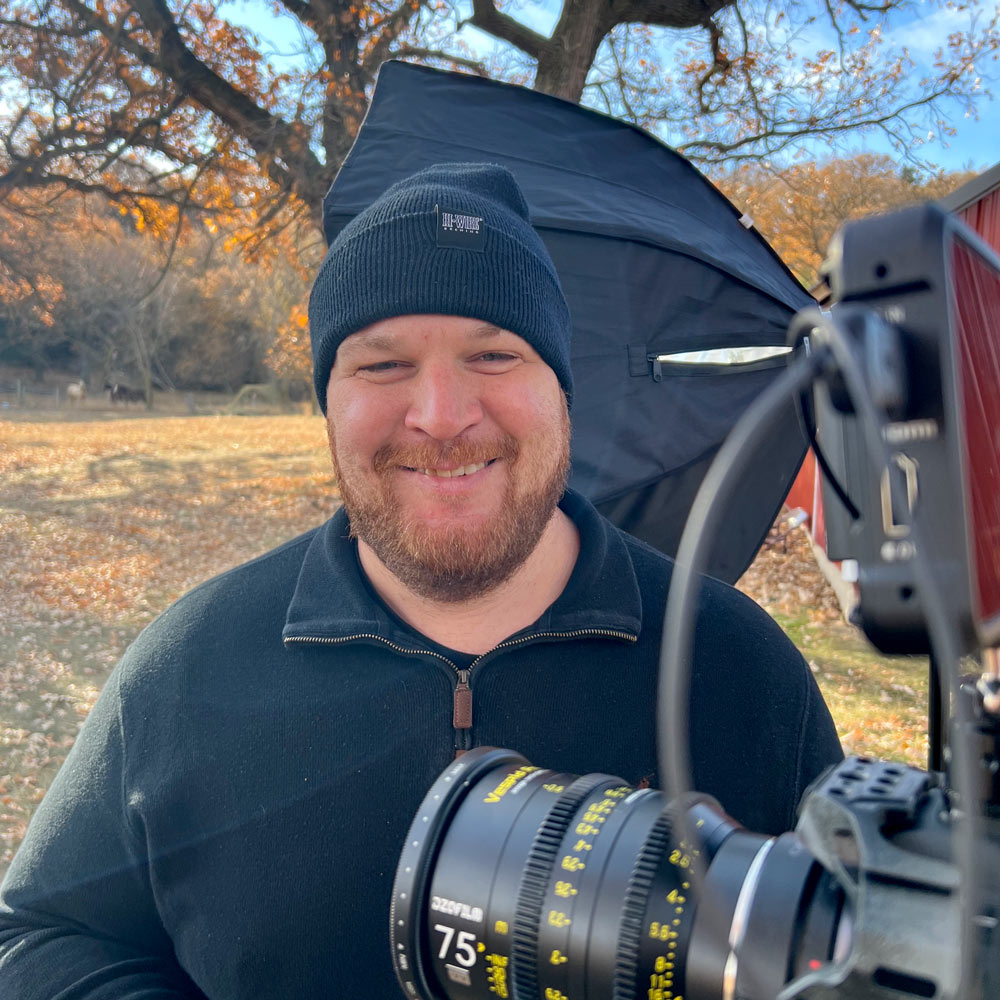 Headshot of Parable Pictures team member T.J. Donaldson smiling and wearing a toboggan on set with his production camera and photography soft box
